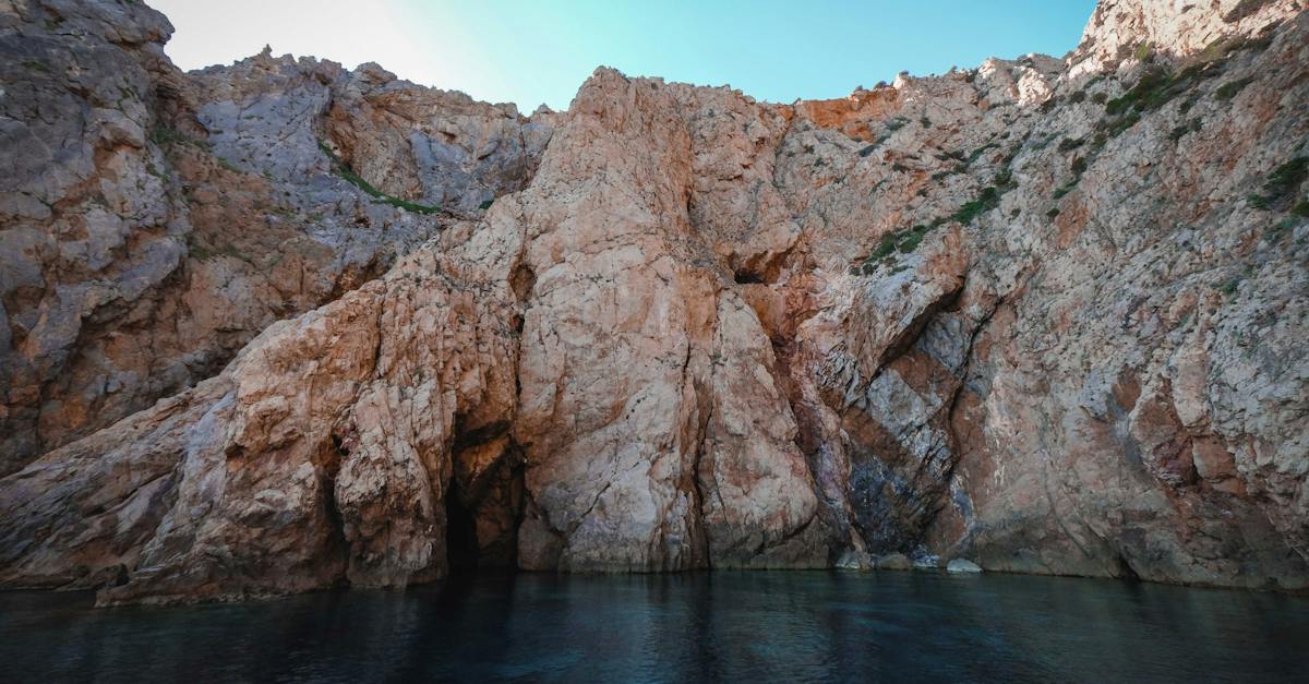 calm-river-flowing-near-rough-rocky-cliffs-with-uneven-surface-against-cloudless-blue-sky-in-nature-4597633