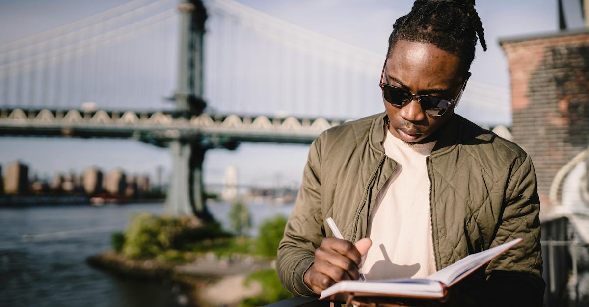 concentrated-young-black-male-checking-schedule-in-notebook-while-standing-on-city-promenade-against-1076940