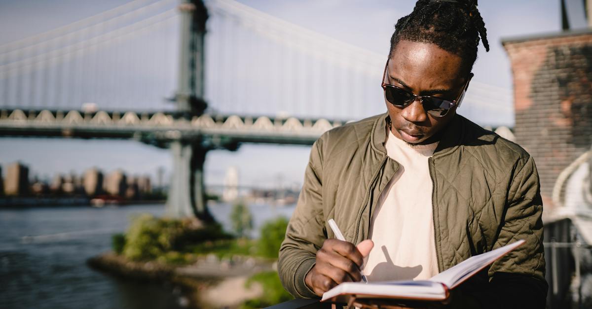 concentrated-young-black-male-checking-schedule-in-notebook-while-standing-on-city-promenade-against-7343755