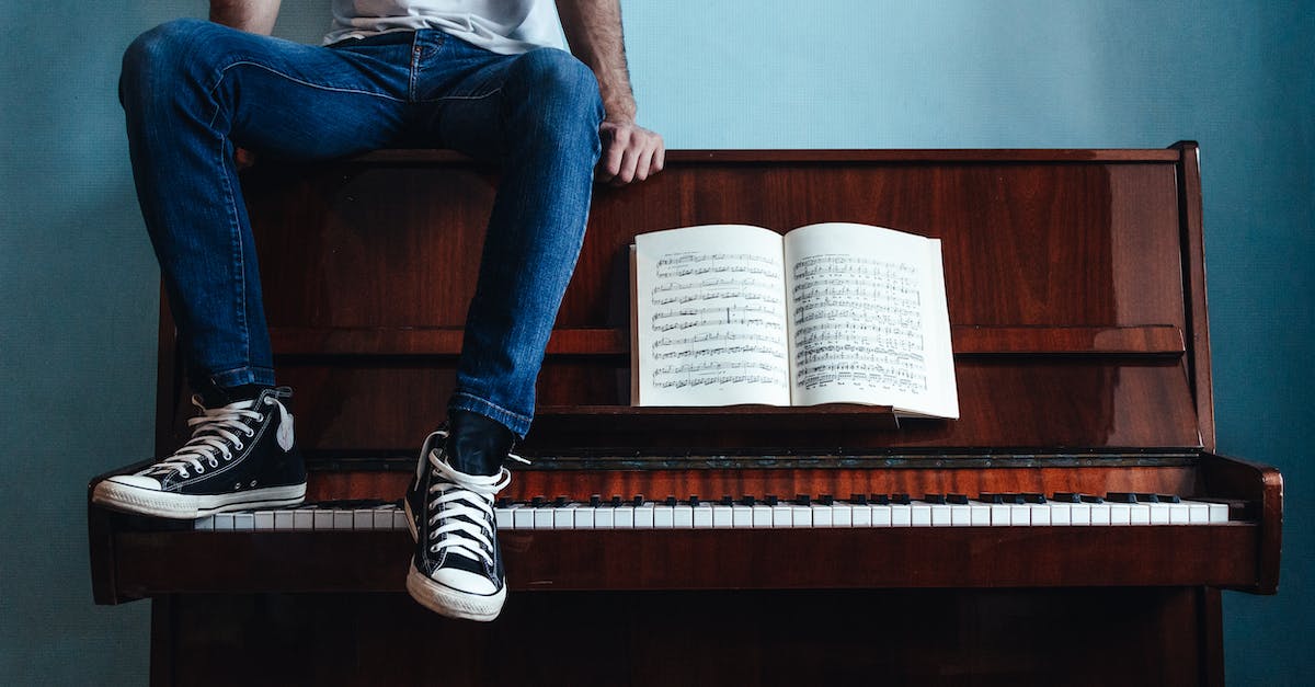 crop-unrecognizable-male-in-trendy-gumshoes-and-jeans-sitting-on-piano-with-sheet-music-in-classroom-1598509