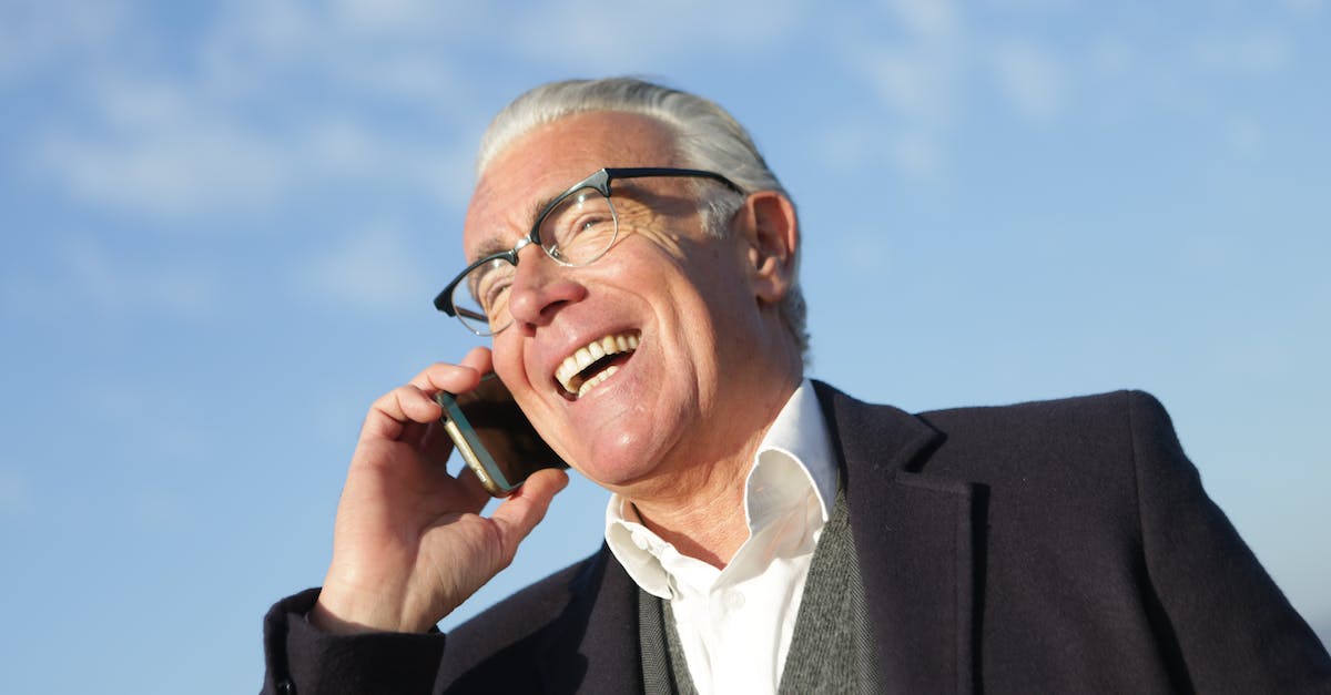 from-below-of-delighted-aged-male-entrepreneur-in-classy-outfit-standing-on-street-and-speaking-on-c-9078159