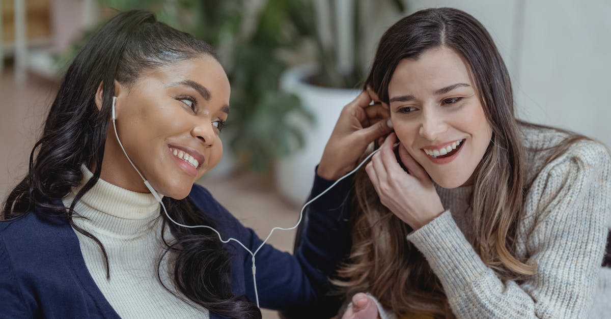 happy-young-african-american-lady-with-smartphone-and-earphones-smiling-and-sharing-music-with-femal-2138235