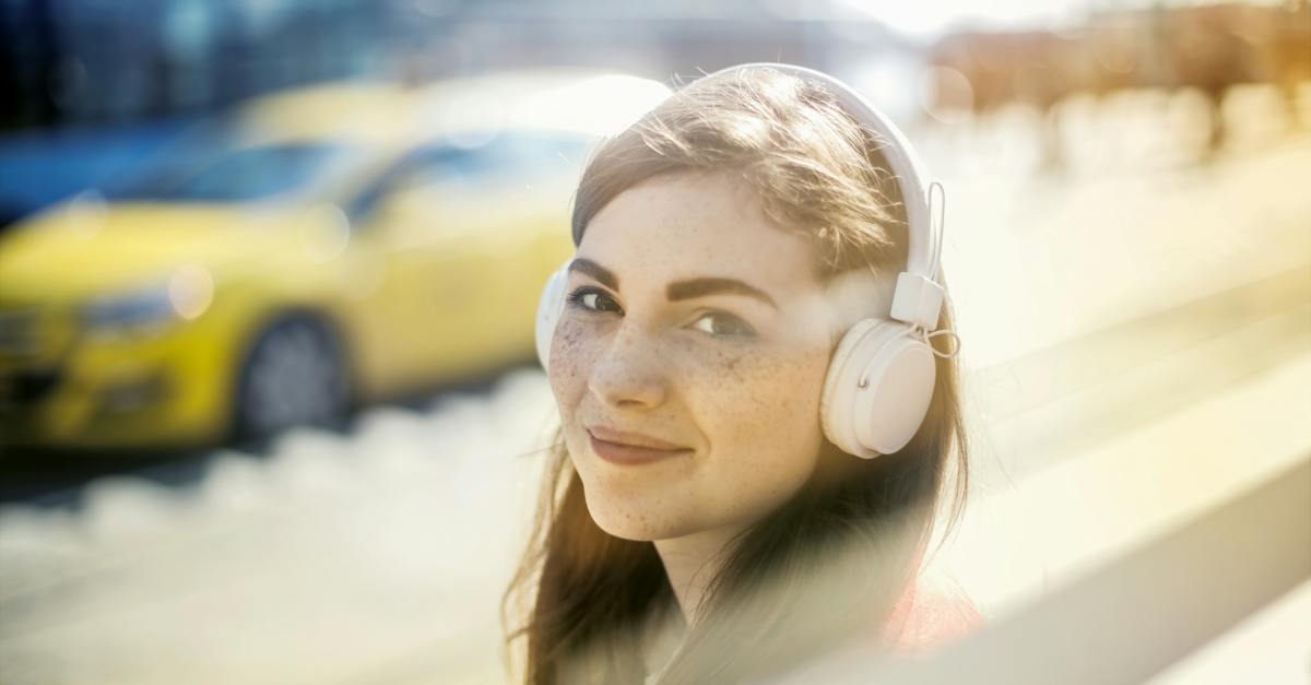 happy-young-woman-in-headphones-listening-to-music-on-street-9197884