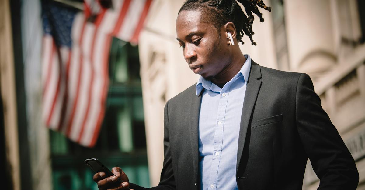 low-angle-of-young-african-american-male-entrepreneur-in-formal-suit-messaging-on-cellphone-with-wir-3307903