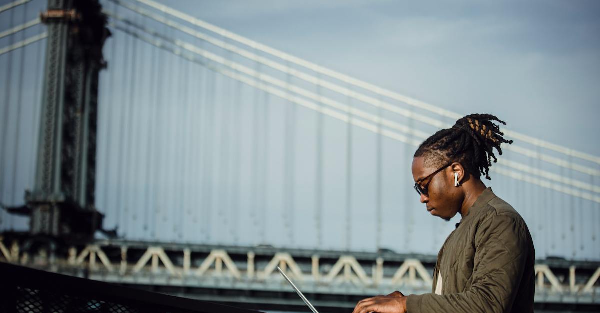 side-view-of-cool-young-african-american-man-with-dreadlocks-in-sunglasses-and-earbuds-working-on-la-6799184