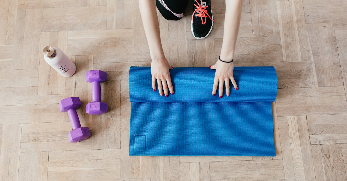 top-view-of-anonymous-female-athlete-in-black-leggings-and-sneakers-unfolding-blue-mat-for-exercisin-4621398