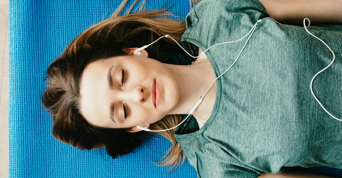 tranquil-woman-resting-on-yoga-mat-in-earphones-at-home-4093379