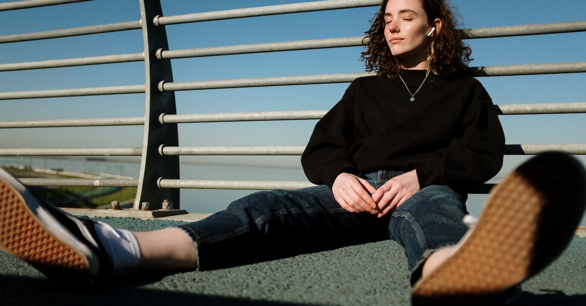 woman-in-black-long-sleeve-shirt-and-blue-denim-jeans-sitting-on-green-grass-field-during-3982872