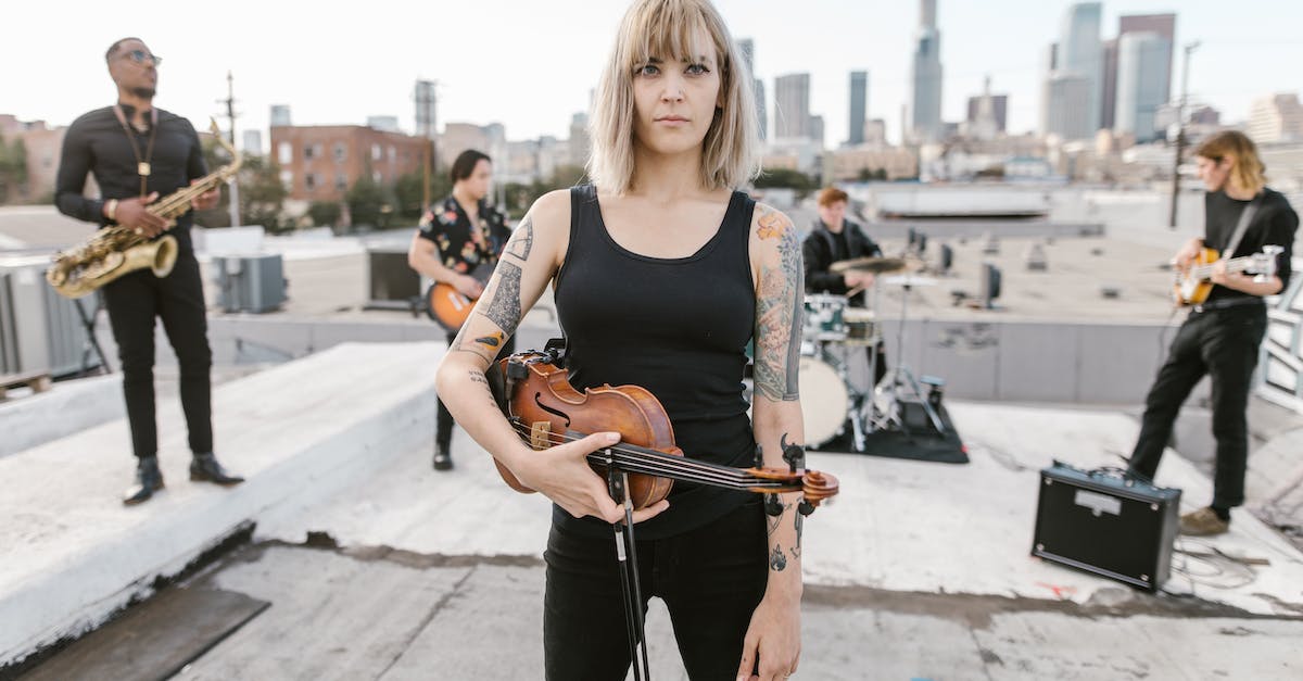 woman-in-black-top-holding-violin-while-standing-on-the-rood-with-music-band-behind-5914055