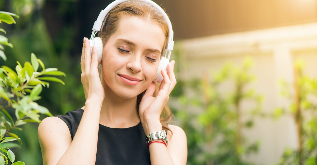 woman-wearing-black-sleeveless-dress-holding-white-headphone-at-daytime-2899045