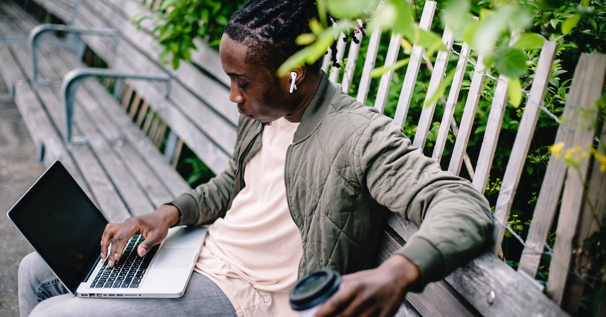 young-black-man-with-coffee-using-laptop-in-park-6736356