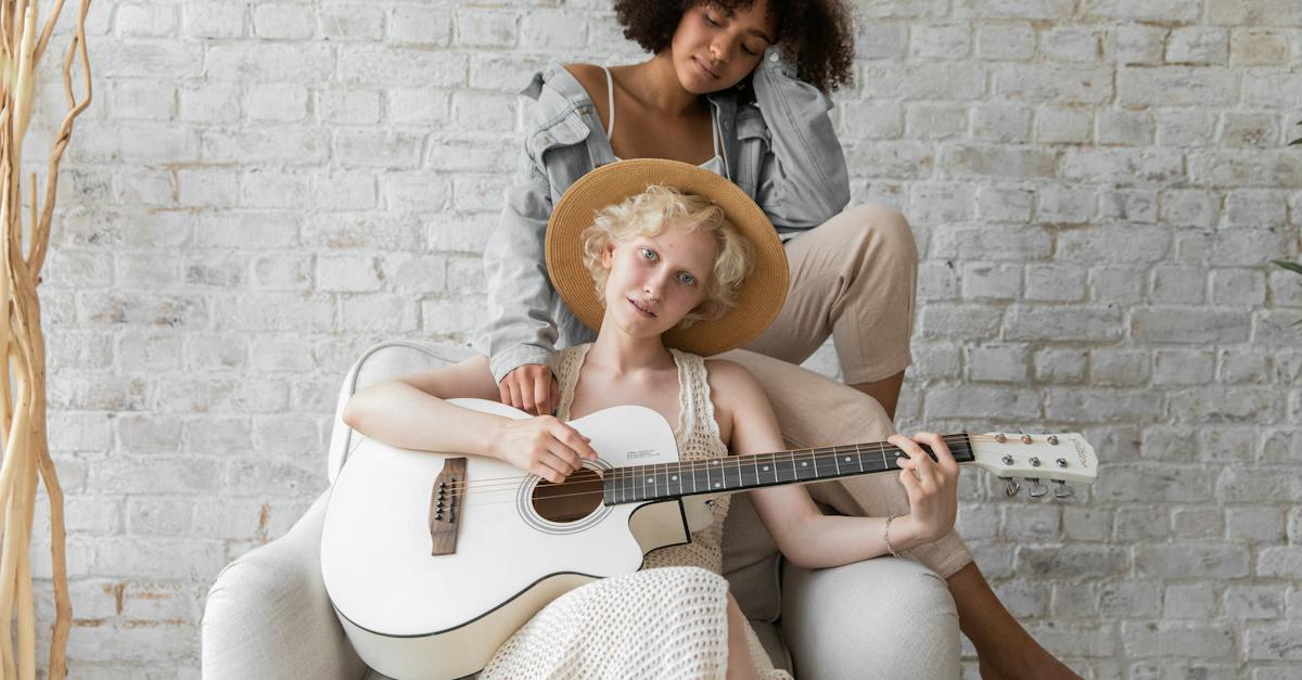young-diverse-homosexual-couple-resting-at-cozy-home-and-playing-acoustic-guitar-against-brick-wall-6595258