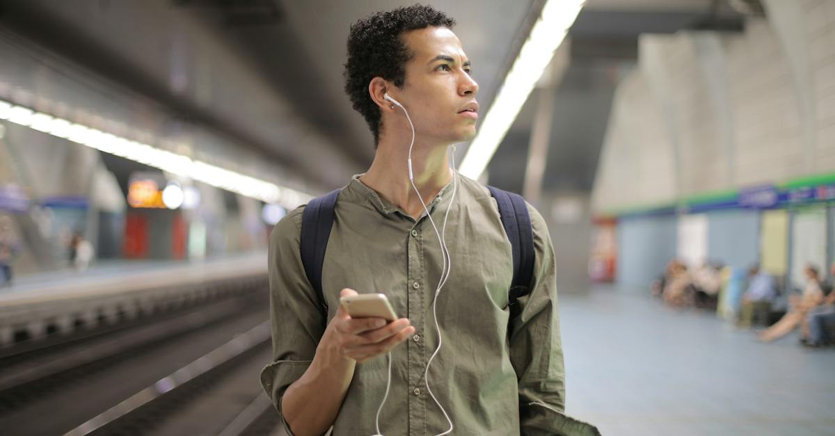 young-ethnic-man-in-earbuds-listening-to-music-while-waiting-for-transport-at-contemporary-subway-st-4465284